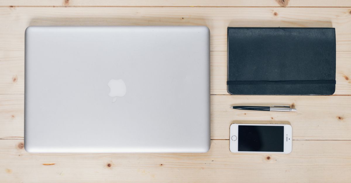 A clean, organized desk featuring a laptop, smartphone, notebook, and pen, ideal for productivity.
